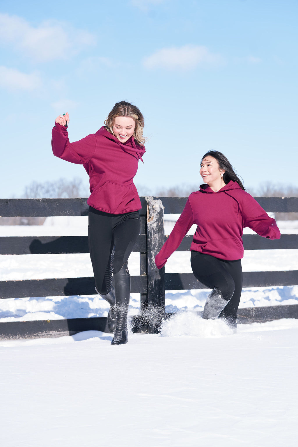 Two people in pink hoodies jumping off a fence in an equestrian setting